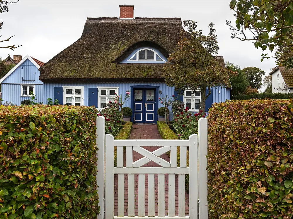 Rohrdachhaus mit weißer Gartenpforte und Hecke