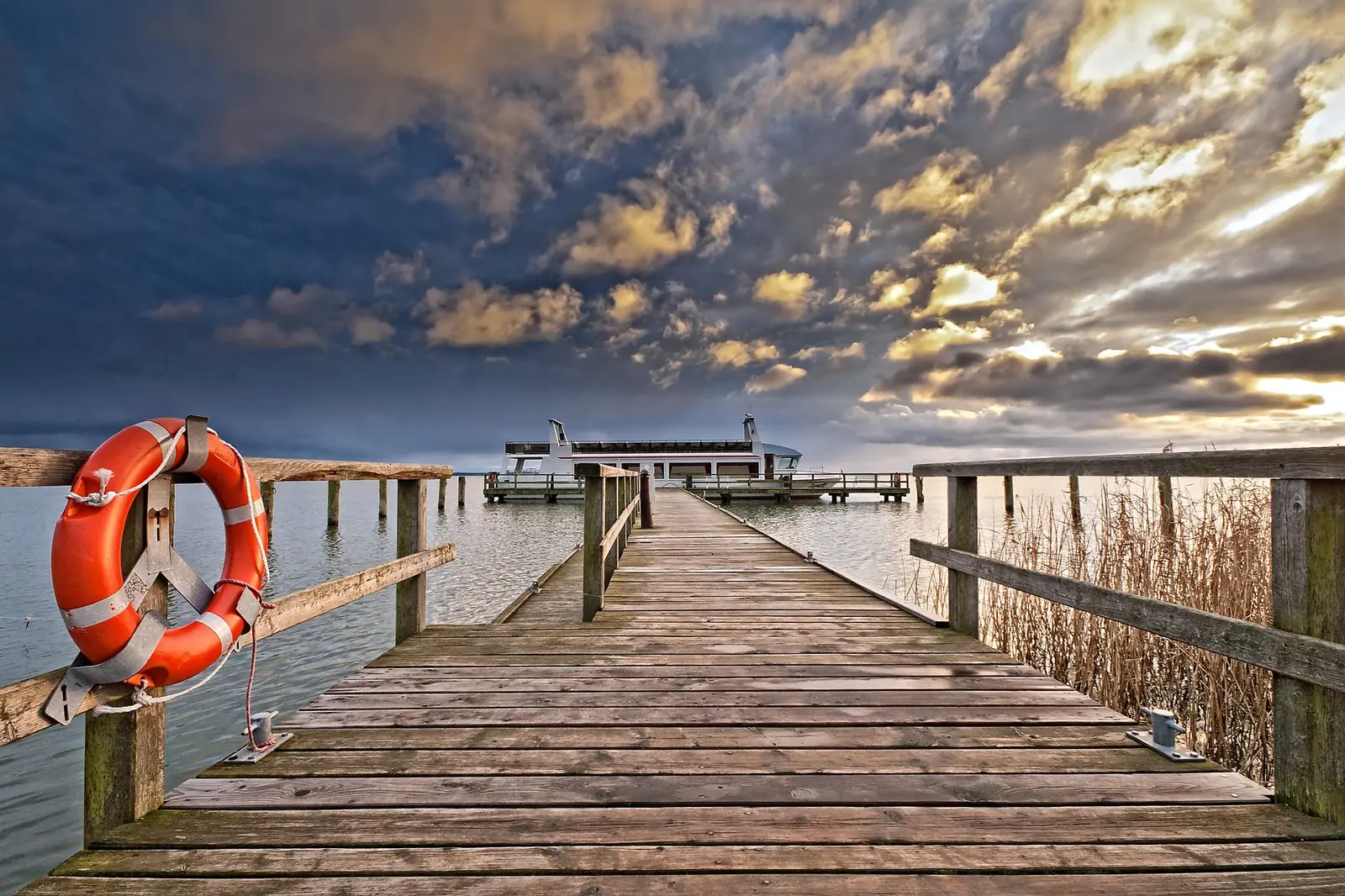 Holzsteg mit Rettungsring und Fahrgastschiff am Ende