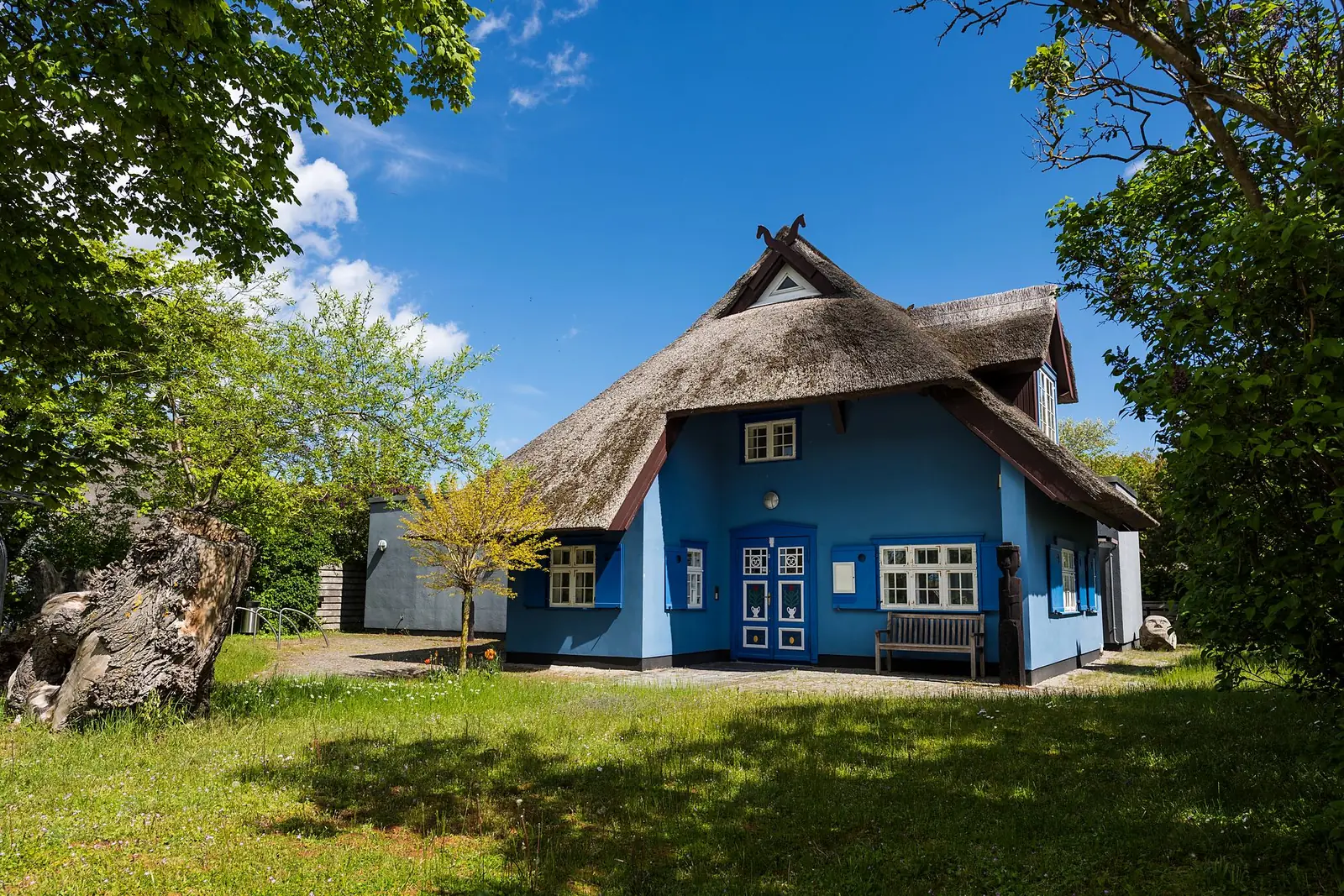 Der Kunstkaten mit Rohrdach und blauer Fassade im Garten