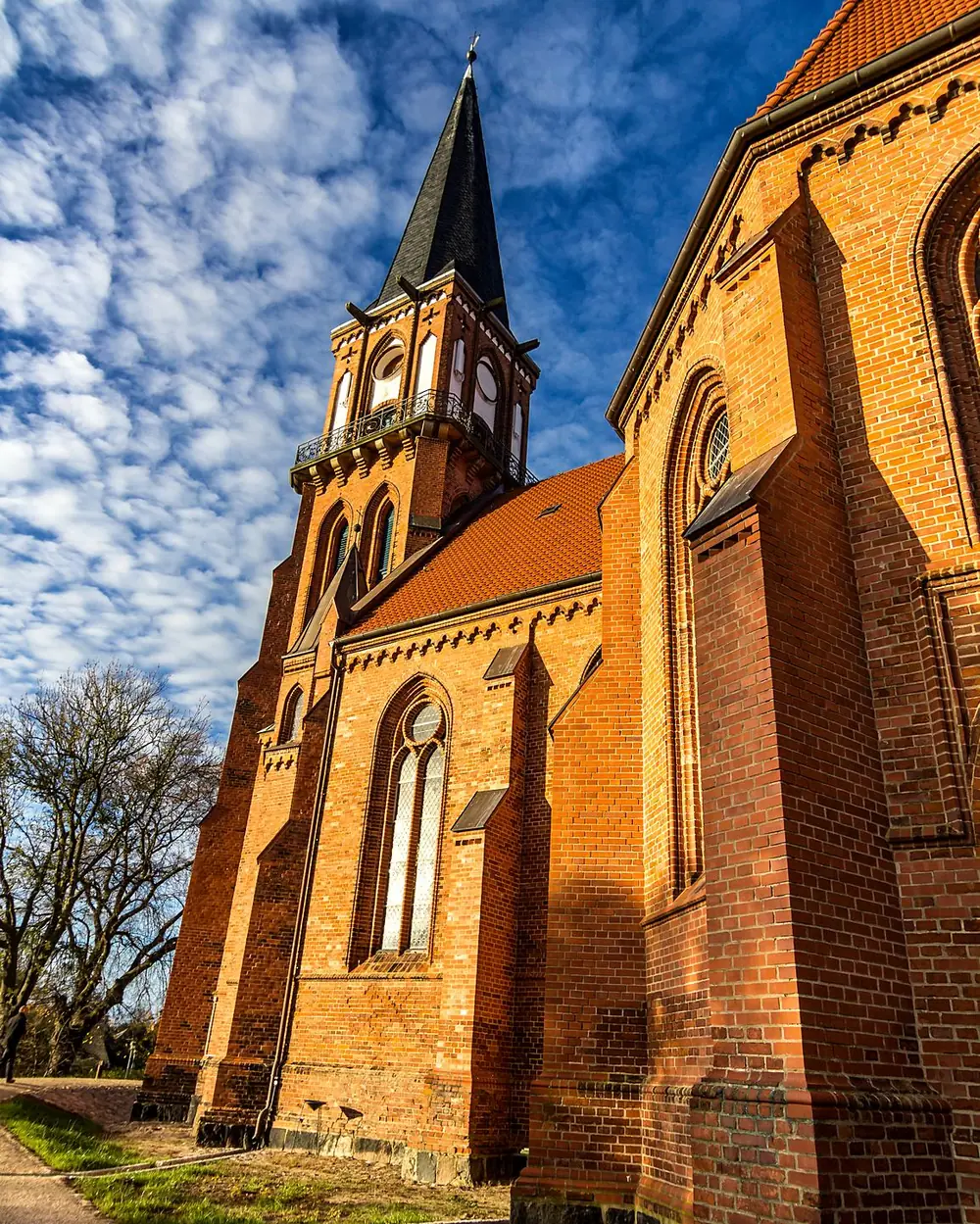Backsteinkirche mit spitzem Turm vor bewegtem Himmel
