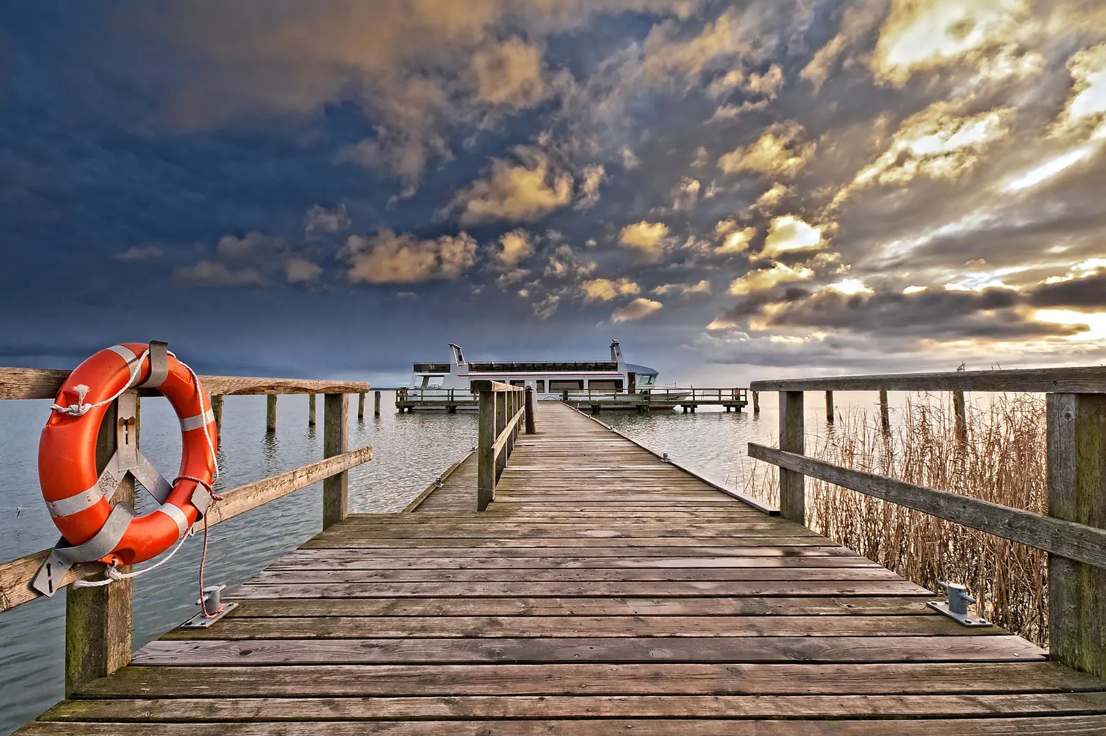 Holzsteg am Bodden mit Rettungsring und Fahrgastschiff